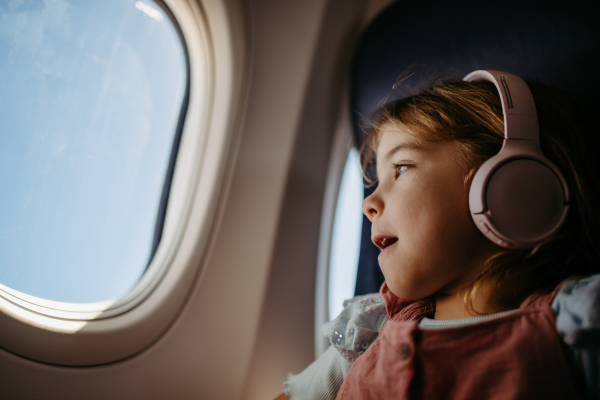 Little girl in airplane listening music and looking out of the window.