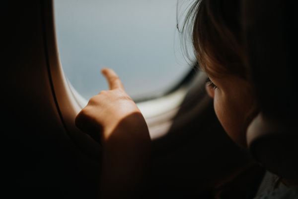 Little girl in airplane listening music and looking out of the window.