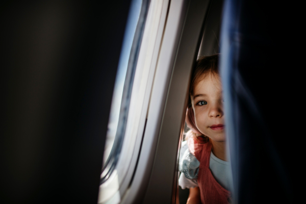 Little curious girl looking through seat in the airplane.