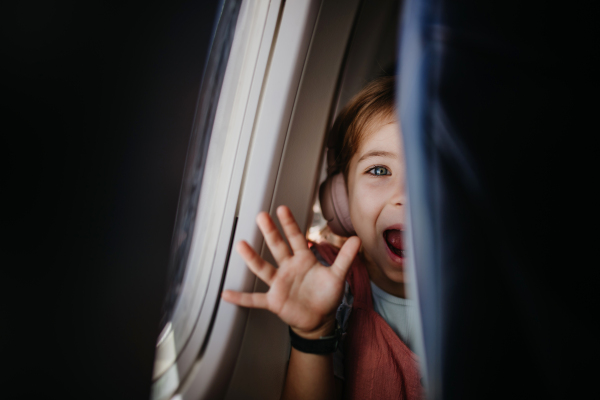 Little curious girl looking through seat in the airplane.