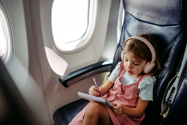 Little girl in an airplane drawing and listening music.