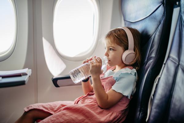 Little girl in airplane listening music and drinking water.