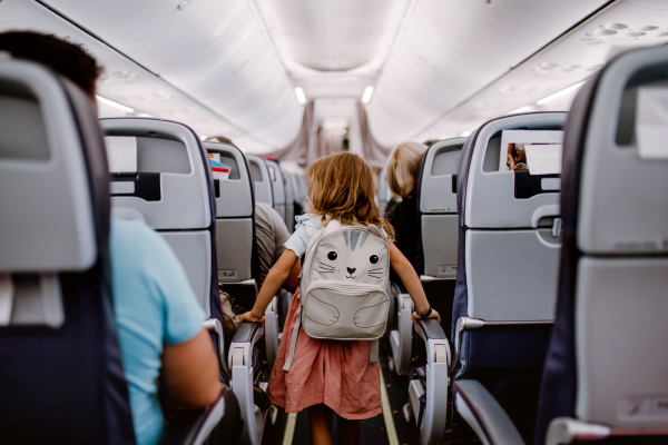 Rear view of little girl with backpack standing in aisle in the plane.