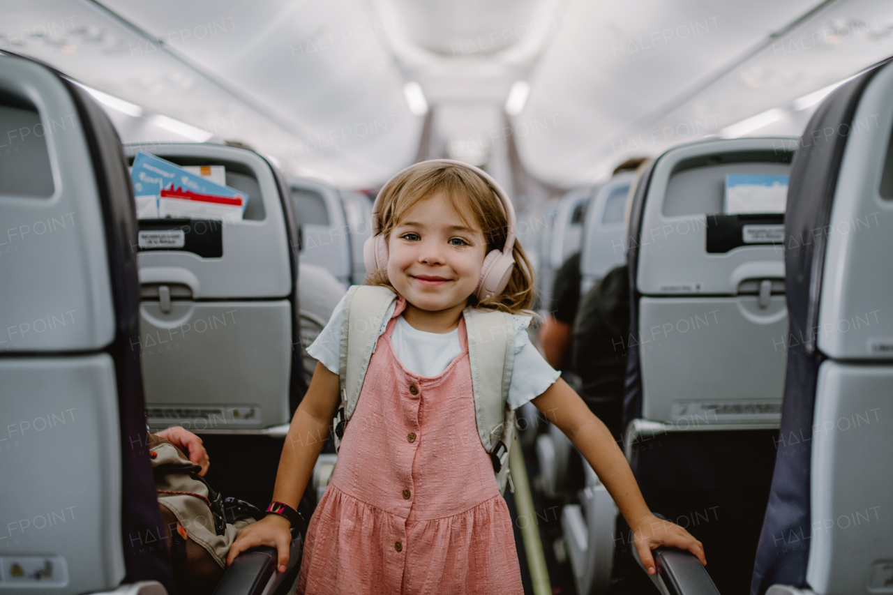 Smiling little girl with backpack standing in aisle in the plane.