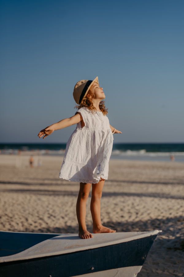 Little girl in summer dress and hat enjoying time at sea during summer vacation.