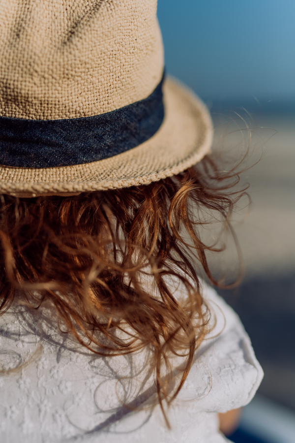 Rear view of little girl in straw hat looking at the ocean.