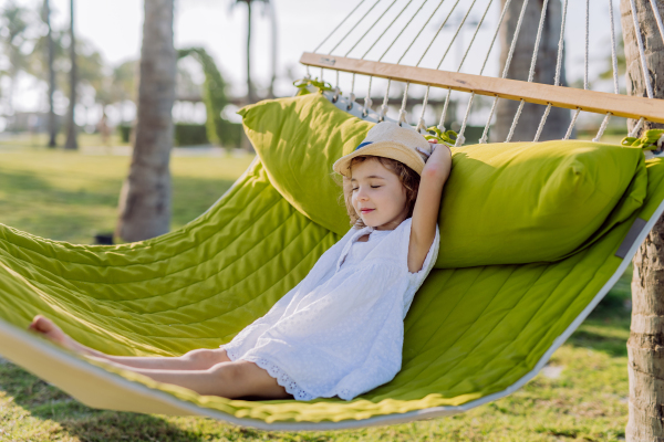 Little girl in straw hat lying in a hammock and enjoying summer exotic vacation.