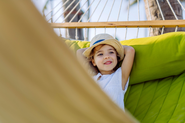 Little girl in straw hat lying in a hammock and enjoying summer exotic vacation.