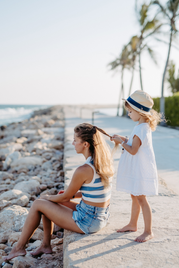 Little girl making hairstyle her mother, enjoying summer time at ocean.