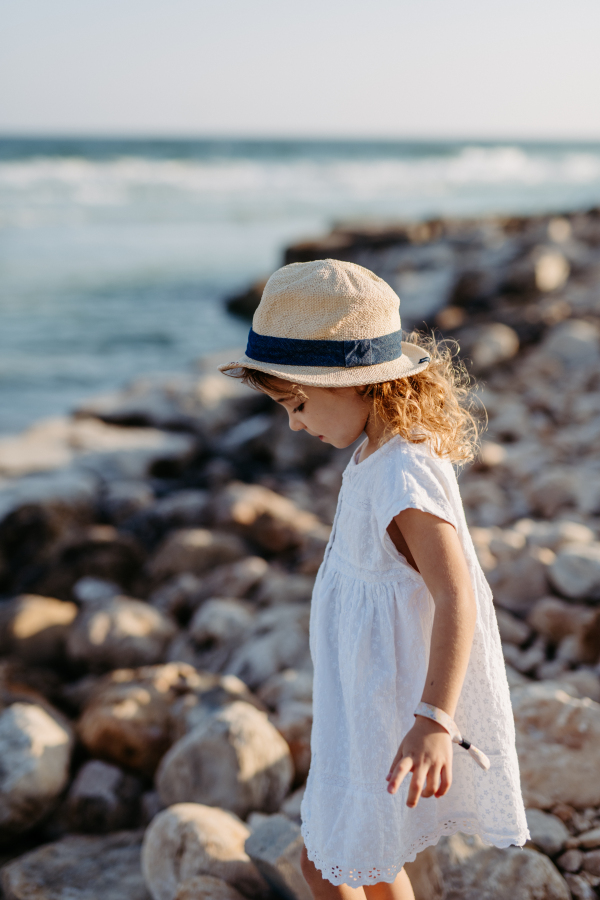 Little girl in summer dress and hat enjoying time at sea during summer vacation.