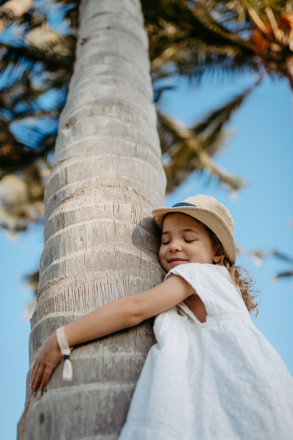 Happy little girl hugging palm tree during the tropical vacation.