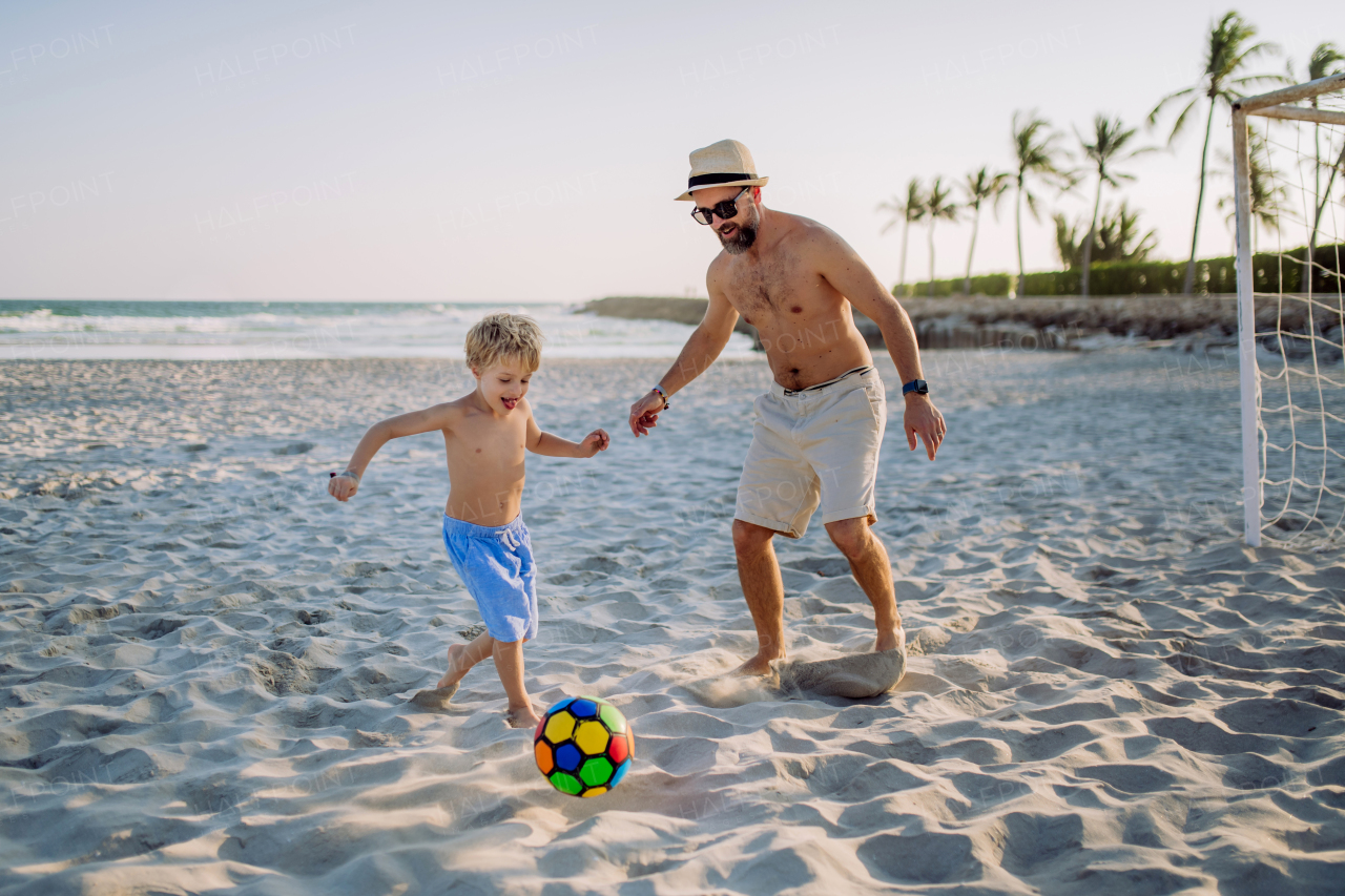 Father with his son plaing football on a beach.