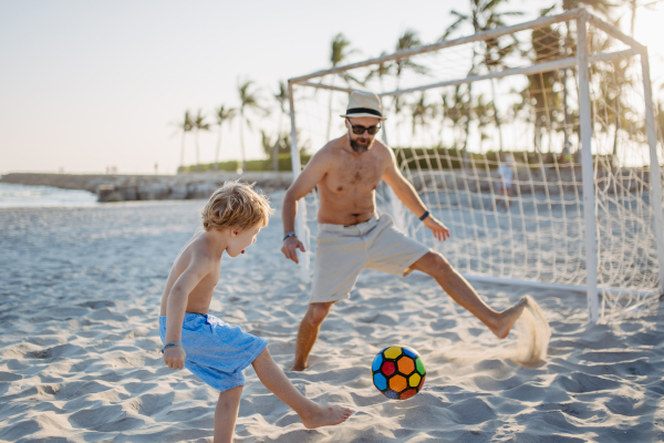 Father with his son plaing football on a beach.