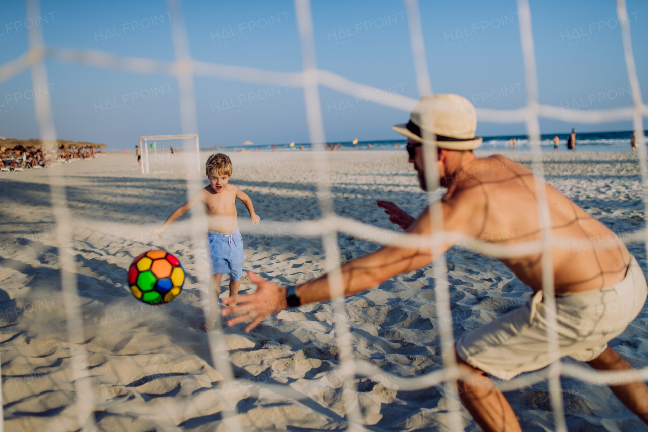 Father with his son plaing football on a beach.