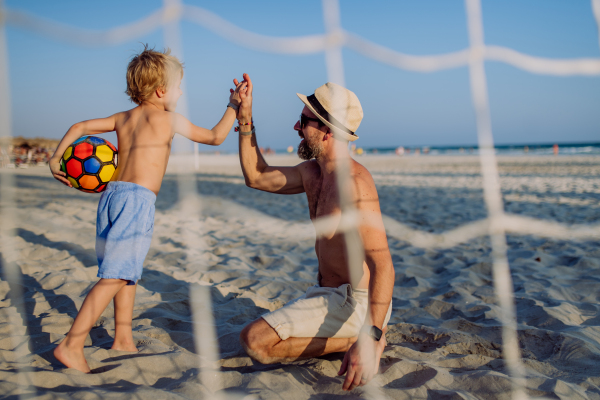 Father with his son plaing football on a beach.