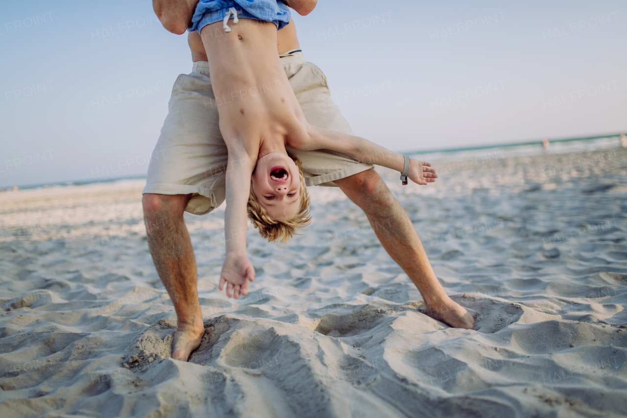 Father holding his son upside down, enjoying summer vacation and having fun.