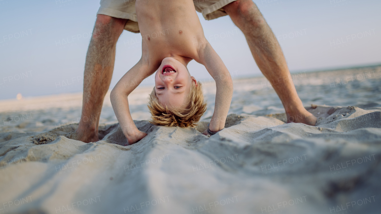 Father holding his son upside down, enjoying summer vacation and having fun.