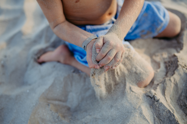 Little boy playing on the beach, sitting in sand.