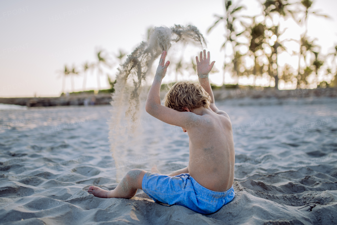 Rear view of little playful boy playing with sand on the beach.