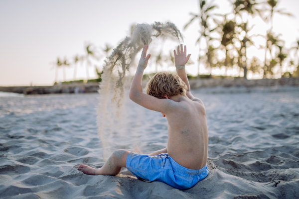 Rear view of little playful boy playing with sand on the beach.