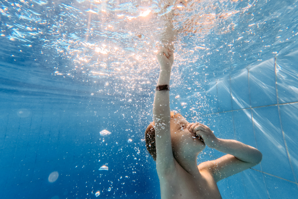 Little boy diving with closed eyes in a swimming pool.