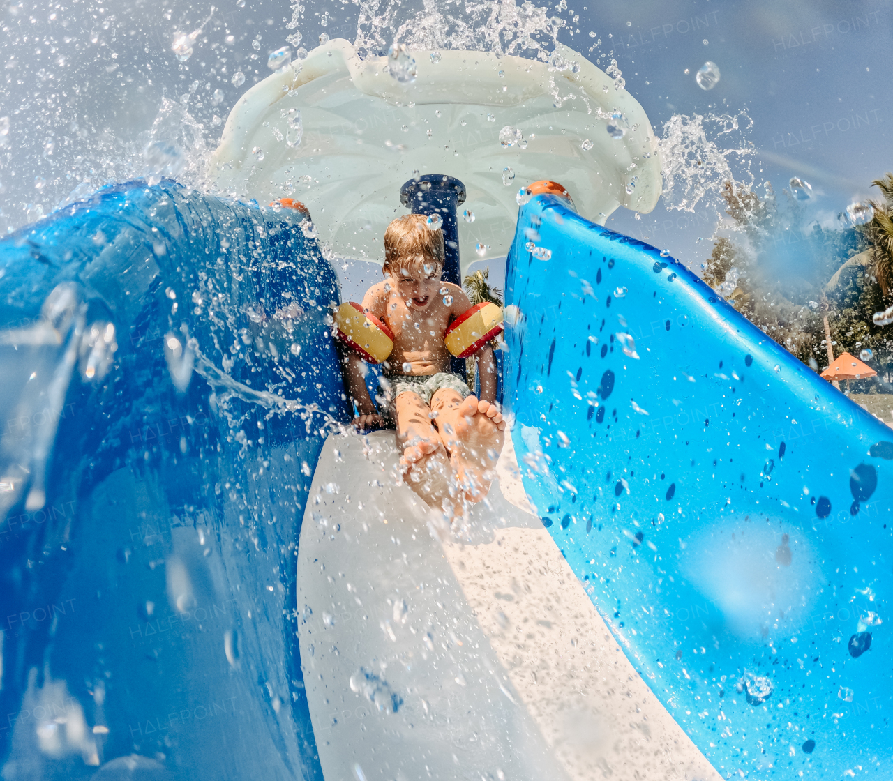 Little boy enjoying water slide during family holiday in exotic country.