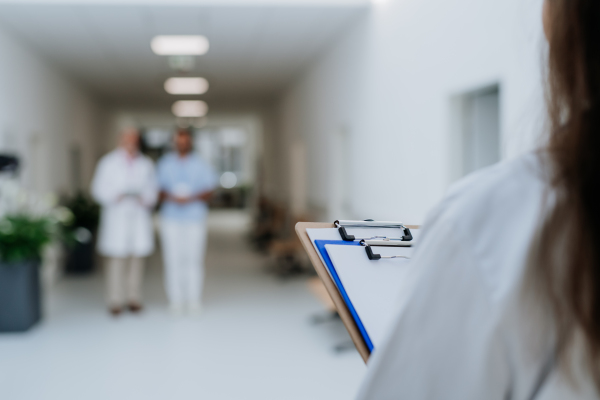 Rear view of young nurse with medical record waiting for older colleagues.