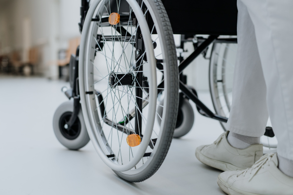 Rear view of caregiver pushing wheelchiar at a corridor in hospital.