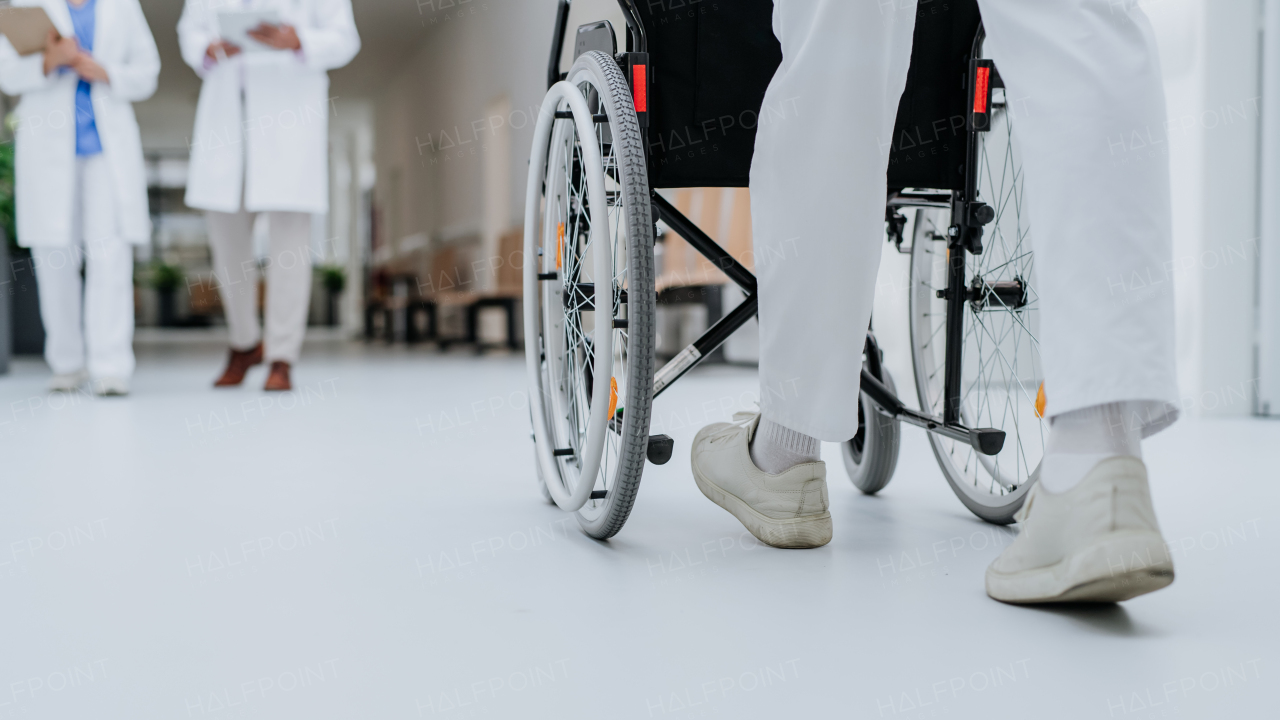 Rear view of caregiver pushing wheelchiar at a corridor in hospital.