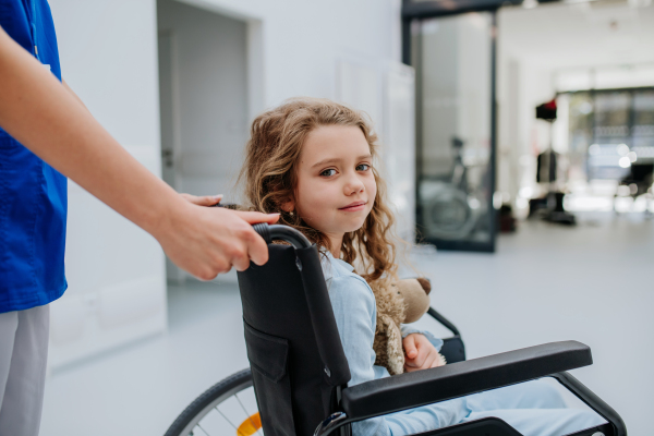 Portrait of little girl with teddy bear sitting on a wheelchair.