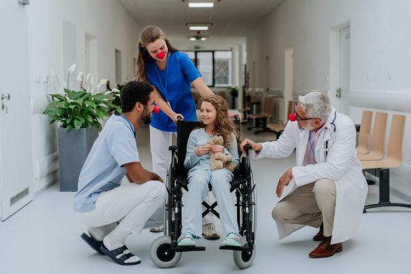 Happy doctors with a clown red noses taking care about little girl.