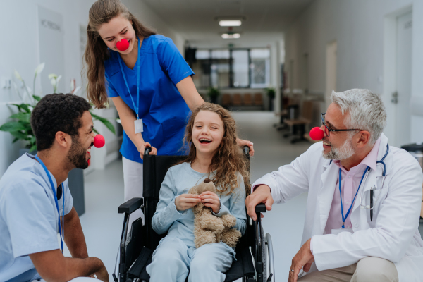 Happy doctors with a clown red noses taking care about little girl.