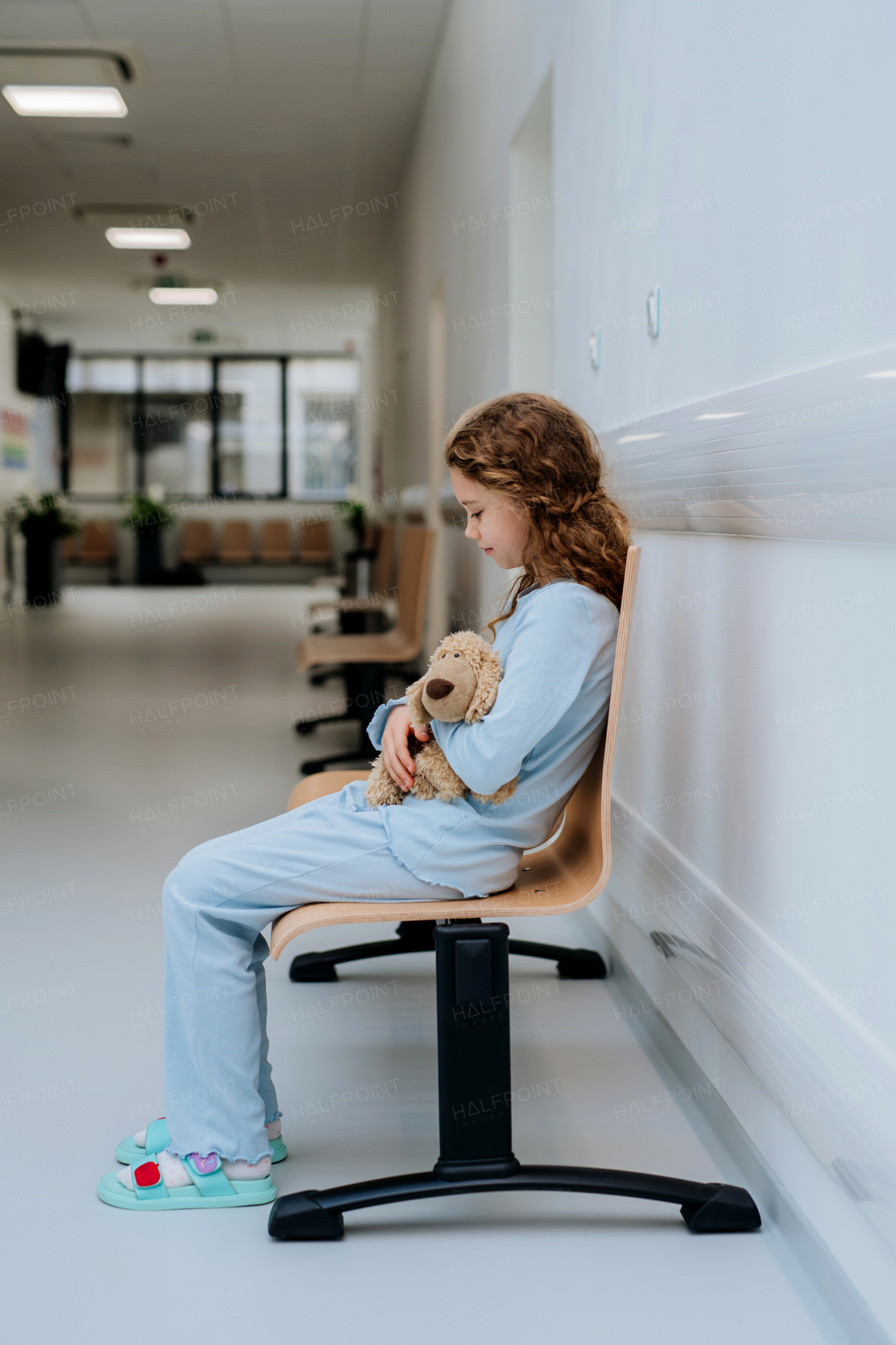 Little girl, patient, sitting alone at a hospital corridor with her teddy bear.