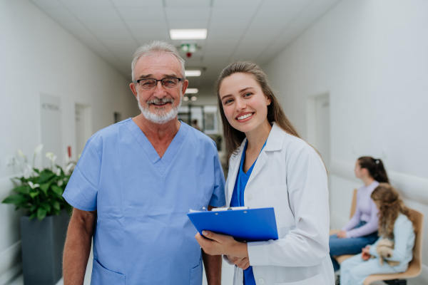 Portrait of elderly doctor with his younger colleague at a hospital corridor. Health care concept.