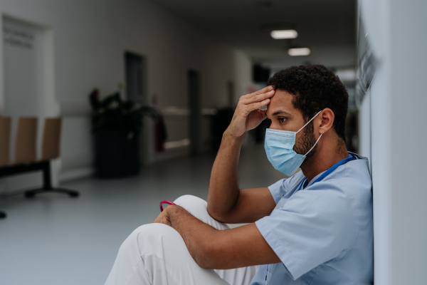 Young distressed doctor sitting at a hospital corridor floor.