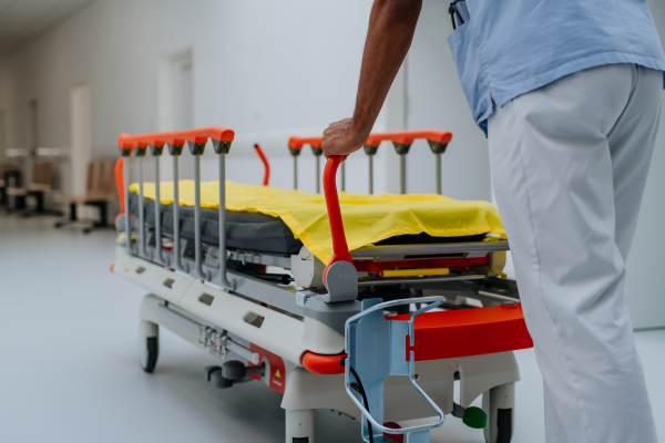 Rear view of caregiver pushing hospital bed at a corridor.