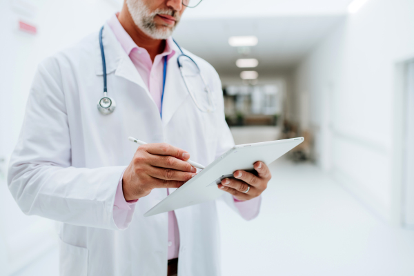 Mid section of mature doctor with digital tablet at a hospital corridor.