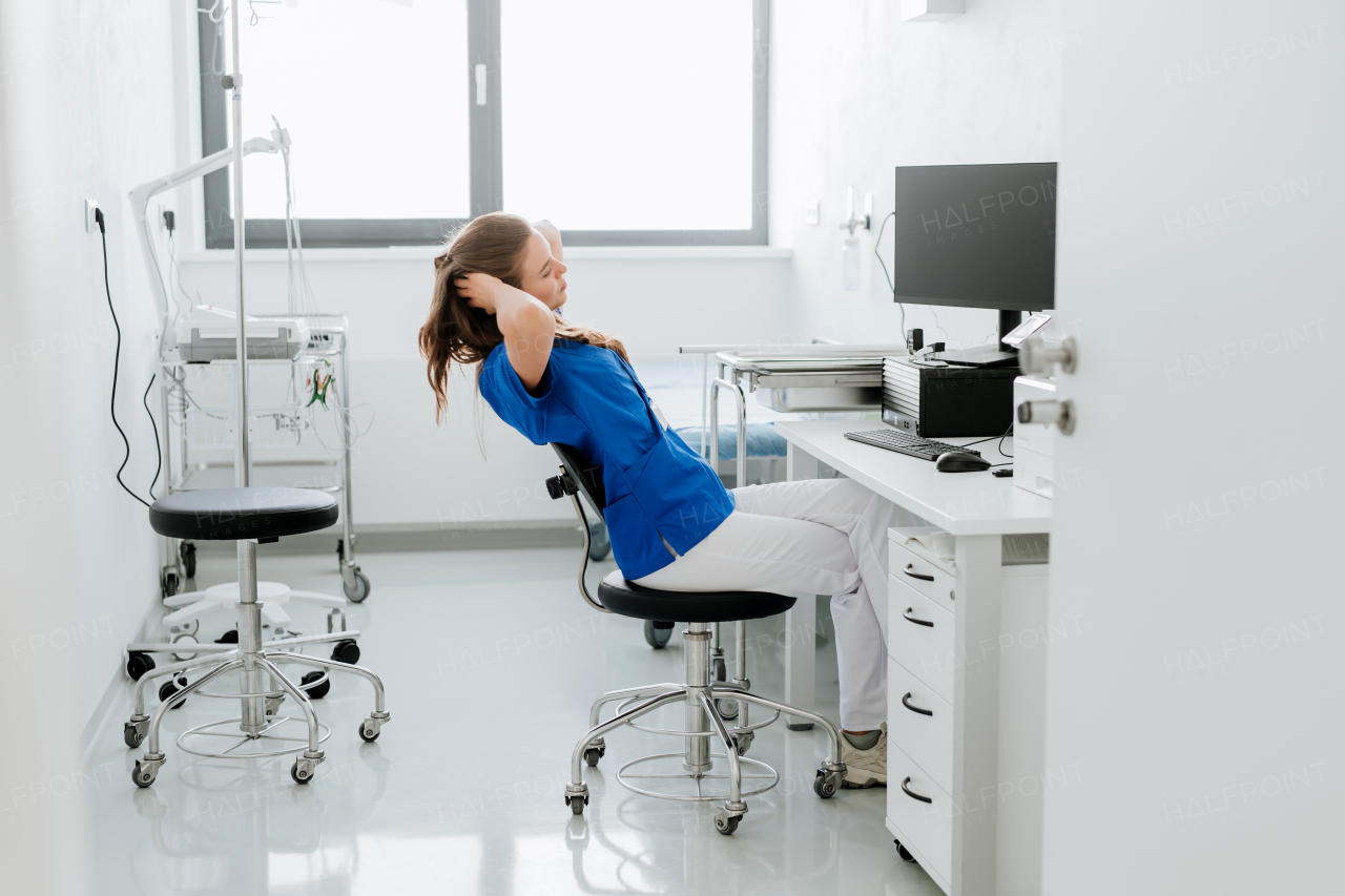 Young woman doctor stretching at a hospital office desk.