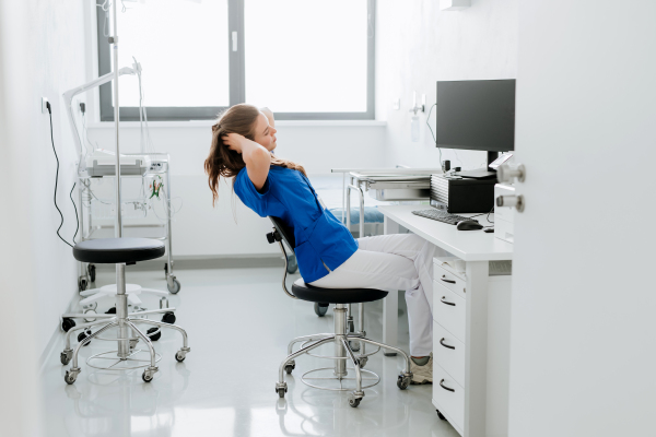 Young woman doctor stretching at a hospital office desk.