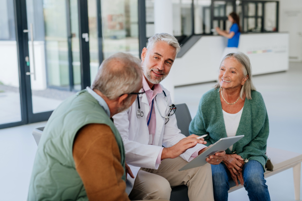 Mature doctor talking with the senior patients at hospital corridor.