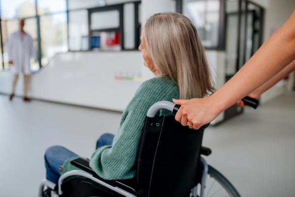 Rear view of hospital worker pushing senior woman on a wheelchair.