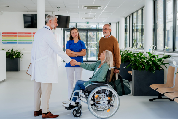 Senior woman on wheelchair meeting a doctor in hospital, shaking hands.