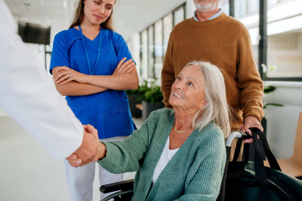 Senior woman on wheelchair meeting a doctor in hospital, shaking hands.