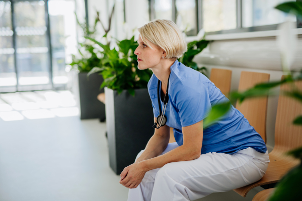 Young pensive doctor sitting at a hospital corridor.