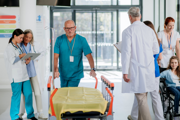 Caregiver pushing hospital bed at a corridor,his colleagues taking care of patients.