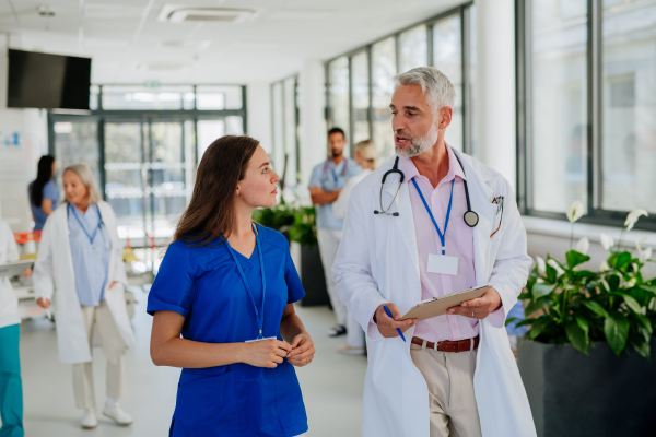 Portrait of elderly doctor with his younger colleague at a hospital corridor. Health care concept.