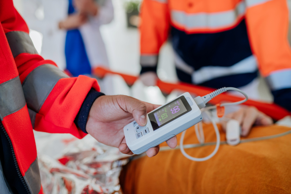 Close-up of rescuers taking care of patient from ambulance, checking an oximeter.