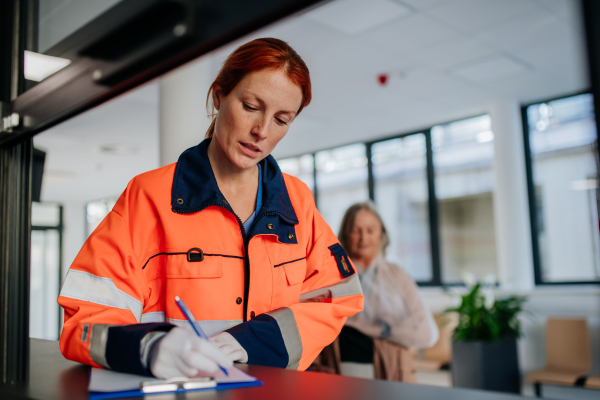 Young woman rescuer filling out paper forms at hospital corridor.