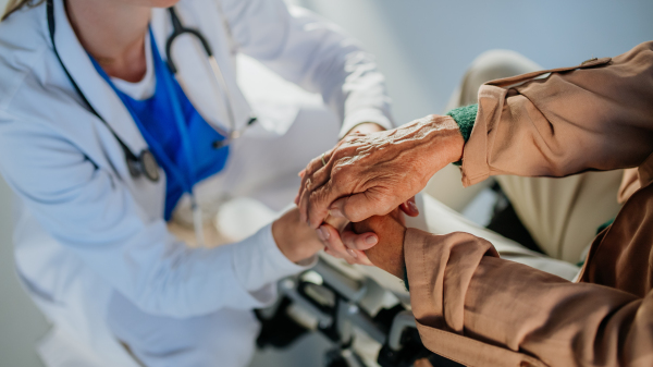 Close-up of young doctor holding hands of patient on wheelchair, consoling her.