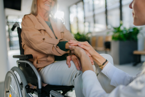 Close-up of young doctor holding hands of patient on wheelchair, consoling her.